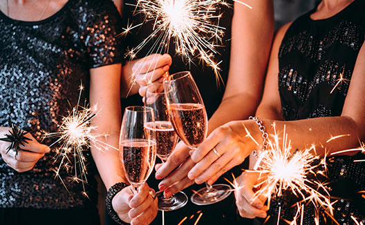 Women in festive attire celebrate with sparkling lights and champagne flutes